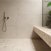 Minimalist bathroom featuring Melange Light concrete-style wall and floor tiles 60 × 60cm, showcasing soft beige concrete-effect tones with subtle texture, paired with terrazzo surfaces, brass fittings, and contemporary architectural styling.
