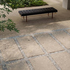 Modern outdoor seating area featuring Melange Sand 20mm thick outdoor Cosmo Stone tile slabs 60 × 120cm, showcasing warm sand-toned terrazzo-inspired detailing, paired with gravel pathways, contemporary landscaping, and minimalist outdoor furniture.