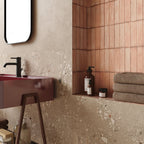 Contemporary bathroom featuring Melange Sand concrete-effect wall and floor tiles 60 × 60cm, showcasing warm sand-toned concrete-inspired detailing with subtle texture, paired with terrazzo accents, blush pink features, and minimalist décor.
