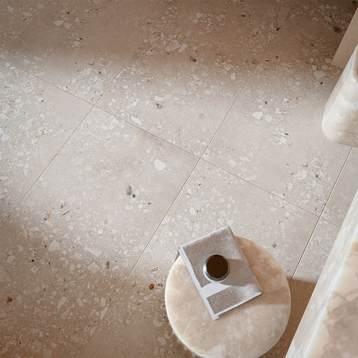 Contemporary interior featuring Melange Sand Cosmo Stone wall and floor tiles 60 × 120cm, showcasing warm sand-toned stone-effect detailing with terrazzo-inspired aggregate texture, paired with soft neutral furnishings and marble accents.