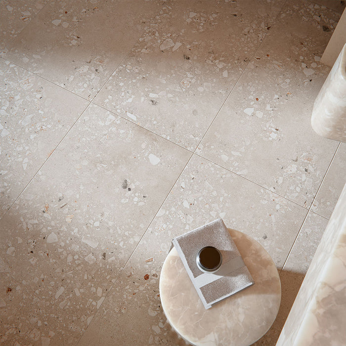 Contemporary interior featuring Melange Sand Cosmo Stone wall and floor tiles 60 × 120cm, showcasing warm sand-toned stone-effect detailing with terrazzo-inspired aggregate texture, paired with soft neutral furnishings and marble accents.