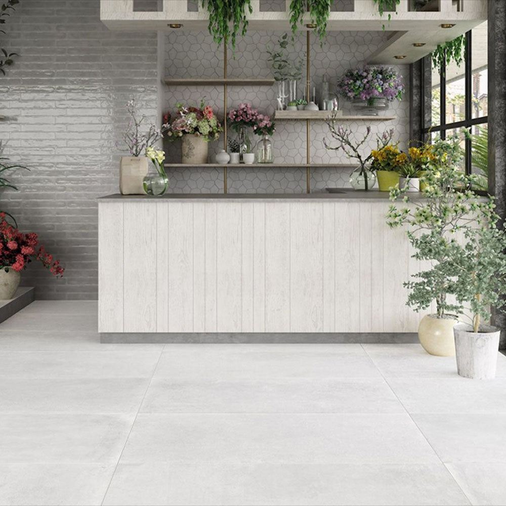 Bright botanical interior featuring Melody Cement White 30 × 60cm concrete-effect porcelain floor tiles, showcasing soft white tones and a subtle industrial texture, paired with natural wood finishes, layered greenery, and light-filled contemporary styling.
