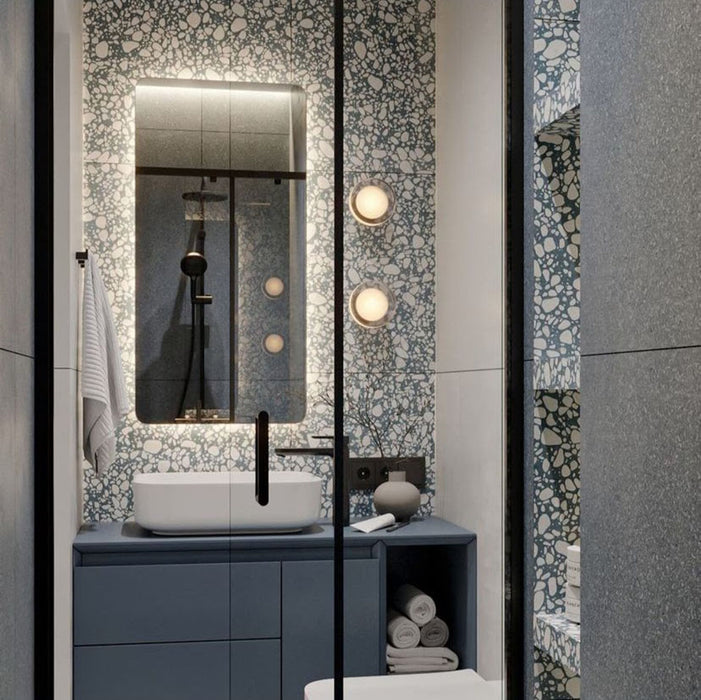 Modern bathroom featuring Melody Pop Blue 60cm x 120cm terrazzo effect porcelain feature wall tiles, paired with large-format grey wall tiles, a blue floating vanity, black brassware and illuminated mirror.