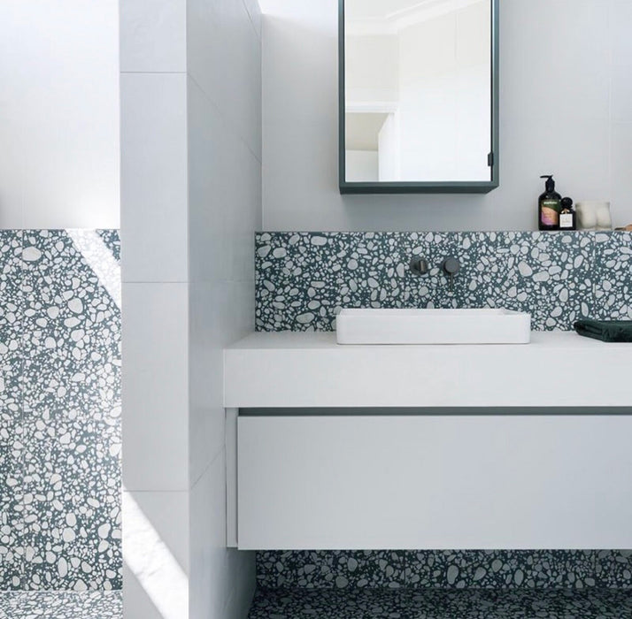 Minimalist bathroom featuring Melody POP Terrazzo Blue 60 × 60cm terrazzo-effect porcelain tiles, showcasing soft white stone fragments across a muted blue base, paired with crisp white surfaces, black fixtures, and clean contemporary styling.