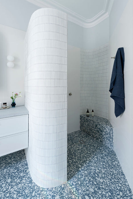 Minimalist bathroom featuring Melody POP Terrazzo Blue 60 × 60cm terrazzo-effect porcelain tiles, showcasing soft white stone fragments across a muted blue base, paired with crisp white surfaces, black fixtures, and clean contemporary styling.