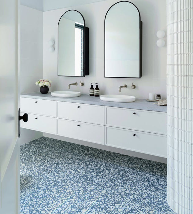 Minimalist bathroom featuring Melody POP Terrazzo Blue 60 × 60cm terrazzo-effect porcelain tiles, showcasing soft white stone fragments across a muted blue base, paired with crisp white surfaces, black fixtures, and clean contemporary styling.