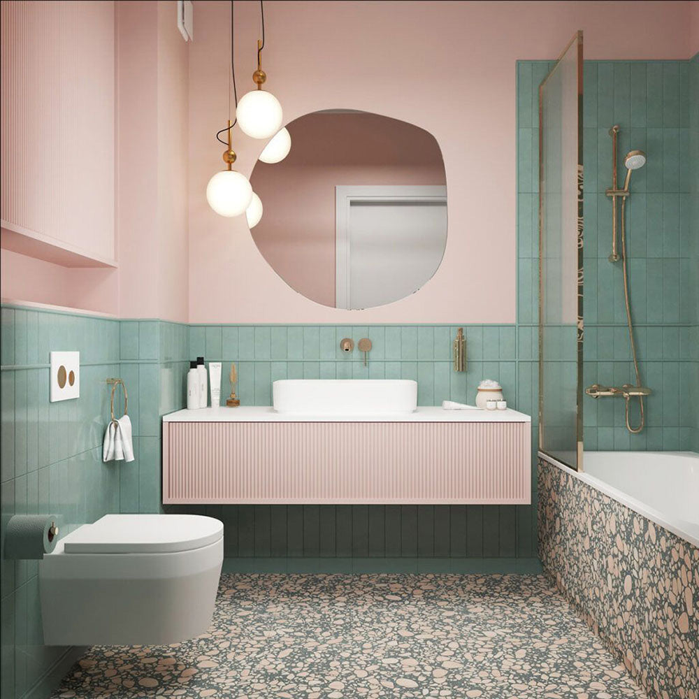 Contemporary bathroom featuring Melody POP Terrazzo Green 60 × 120cm terrazzo-effect porcelain floor tiles, combining blush pink stone fragments with a muted green base, paired with pastel pink walls, glossy green wall tiles, and brushed brass fittings for a playful retro-inspired interior.