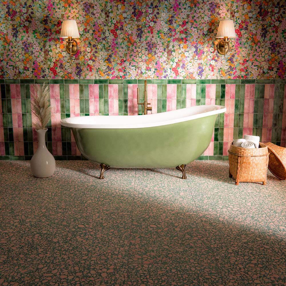Bathroom featuring Melody POP Terrazzo Green 60 × 60cm terrazzo-effect porcelain floor tiles, showcasing a playful green and pink speckled design, paired with striped glossy wall tiles, floral wallpaper, and a sage green freestanding bath for a bold maximalist-inspired interior.