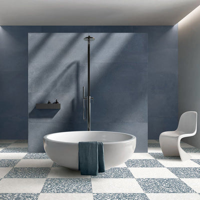 Contemporary bathroom featuring Melody POP Terrazzo White 60 × 60cm terrazzo-effect porcelain floor tiles, laid in a bold blue and white chequerboard design and paired with deep blue wall tiles, a freestanding bath, and minimalist fittings for a striking modern interior.