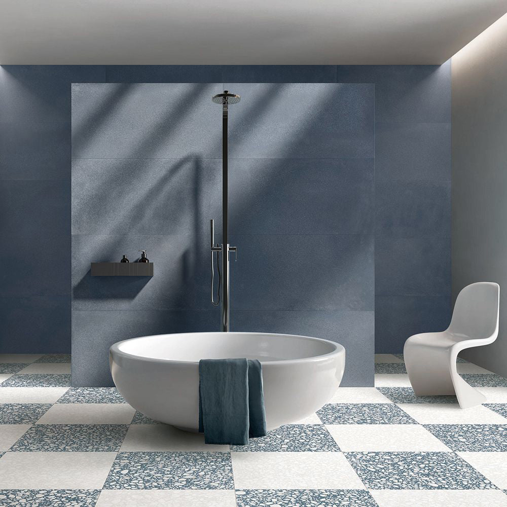Contemporary bathroom featuring Melody POP Terrazzo White 60 × 60cm terrazzo-effect porcelain floor tiles, laid in a bold blue and white chequerboard design and paired with deep blue wall tiles, a freestanding bath, and minimalist fittings for a striking modern interior.