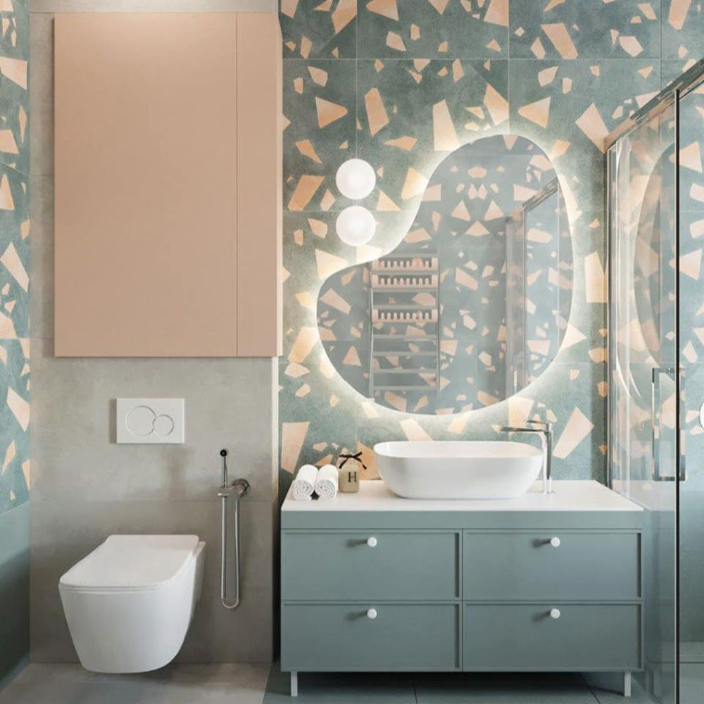 Contemporary bathroom featuring Melody ROCK Terrazzo Green 60 × 120cm terrazzo-effect porcelain wall tiles, showcasing oversized blush pink marble-style fragments against a deep green-grey base, paired with pastel green cabinetry and soft lighting for a playful modern interior.