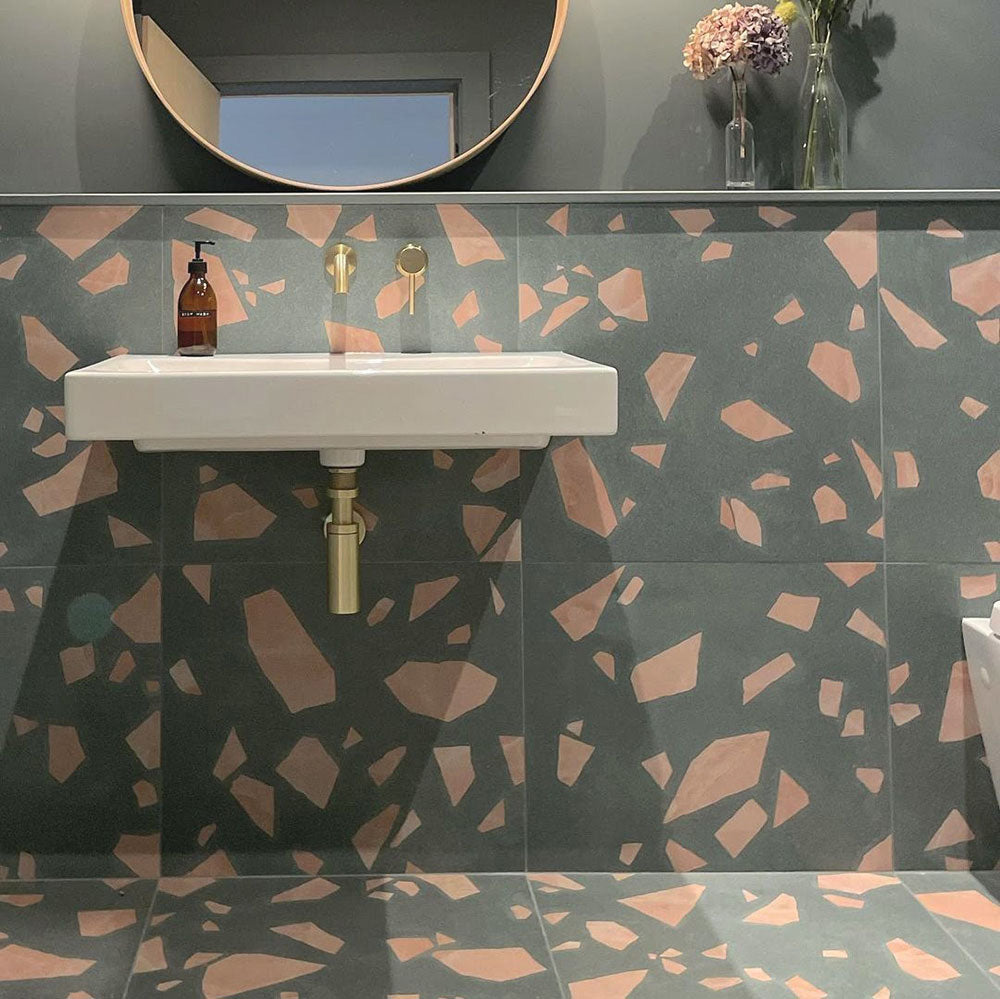Bathroom featuring Melody ROCK Terrazzo Green 60 × 60cm terrazzo-effect porcelain wall and floor tiles, combining oversized blush pink stone fragments with a deep green base, paired with brass fittings and dark painted walls for a bold contemporary interior.