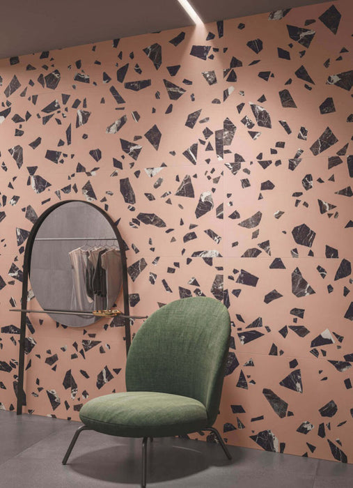 Contemporary interior featuring Melody ROCK Terrazzo Pink 60 × 60cm porcelain wall tiles, designed with oversized black marble-effect fragments set against a soft pink background, creating a bold terrazzo-inspired statement paired with modern furniture and deep charcoal flooring.