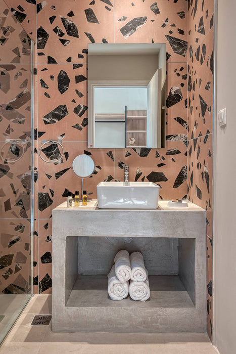 Modern bathroom featuring Melody ROCK Terrazzo Pink 60 × 60cm porcelain wall tiles, showcasing oversized black marble-effect fragments across a warm pink terrazzo-inspired surface, paired with concrete styling, minimalist fittings, and crisp white sanitaryware for a bold contemporary finish.