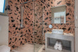 Modern bathroom featuring Melody ROCK Terrazzo Pink 60 × 60cm porcelain wall tiles, showcasing oversized black marble-effect fragments across a warm pink terrazzo-inspired surface, paired with concrete styling, minimalist fittings, and crisp white sanitaryware for a bold contemporary finish.