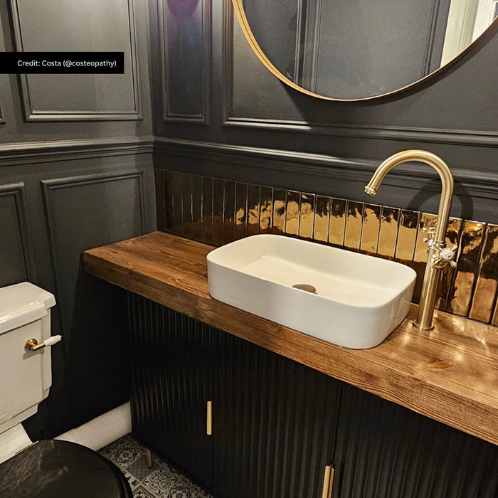 Stylish cloakroom featuring Midas Antique Gold Vintage Crackle wall tiles in a 5cm x 25cm format, paired with dark panelled walls, a timber vanity unit, brass fittings and patterned floor tiles.