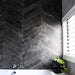 Lifestyle image of Monzo Stone Chevron Nite 10x53cm dark chevron porcelain wall tiles in deep charcoal tones, featuring subtle stone-effect texture and delicate veining, styled within a contemporary bathroom with dramatic contrast and modern black accents.