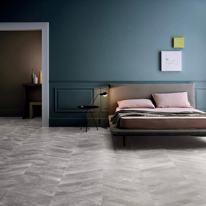 Bedroom featuring Monzo Stone Chevron Titanium 10x53cm stone-effect porcelain chevron floor tiles in soft grey tones, styled with deep blue walls, modern furniture, and subtle natural-style veining for a contemporary interior look.