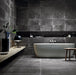 Lifestyle image of Monzo Stone Nite 30x60cm dark stone-effect porcelain wall and floor tiles, featuring rich charcoal tones, subtle veining and varied natural stone-inspired texture, styled within a contemporary bathroom with matte black accents and minimalist décor.