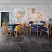 Lifestyle image of Monzo Stone Nite 60x60cm dark stone-effect porcelain floor tiles in deep charcoal tones, featuring subtle veining and varied natural texture, styled within a contemporary café interior with industrial-inspired décor and warm wood furnishings.