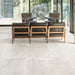 Living room featuring Monzo Stone Silk 60x60cm stone-effect porcelain floor tiles in soft ivory tones, styled with black leather lounge chairs, warm wood furniture, and floor-to-ceiling glazing for a modern interior look.