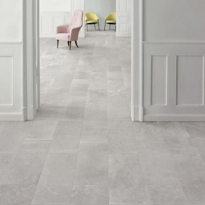 Interior featuring Monzo Stone Silver 30x60cm stone-effect porcelain floor tiles in soft silver-grey tones, styled with white panelled walls, pastel accent chairs, and subtle natural-style veining for a contemporary interior look.