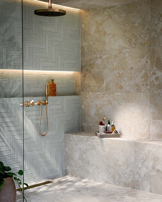 Bathroom featuring Nomad Mint Green Brick 6x24.6cm industrial-style wall tiles, laid in a herringbone pattern and showcasing a glossy mint green finish, paired with brass shower fittings, recessed shelving and warm ambient lighting.