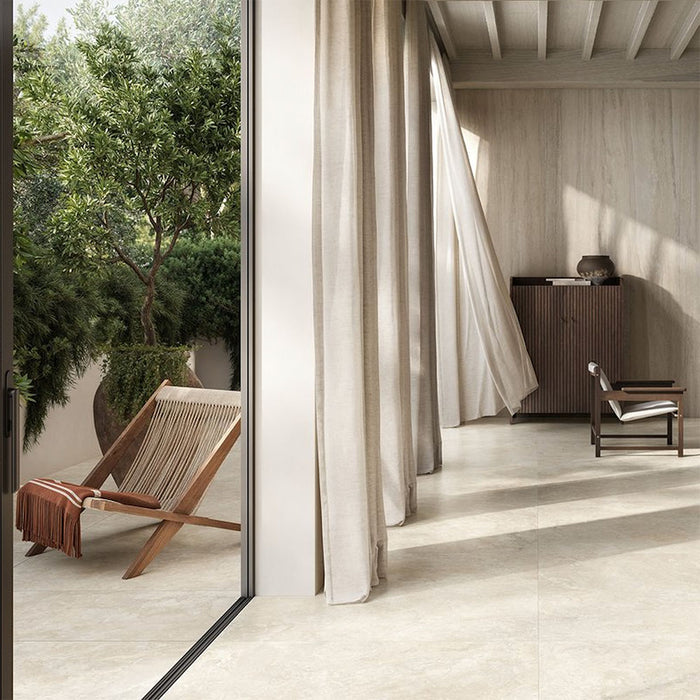 Living room featuring Nucetto Travertine 60x60cm wall and floor tiles, showcasing a soft travertine effect in warm cream and beige tones, extending seamlessly from the interior to the outdoor terrace for a calm, contemporary indoor-outdoor design.