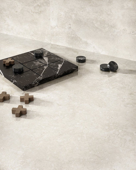 Lifestyle image featuring Nucetto Travertine 60x60cm wall and floor tiles, showcasing soft travertine effect detailing in warm cream and beige tones, paired with a black marble chess set and natural wood accents for a calm, contemporary interior.