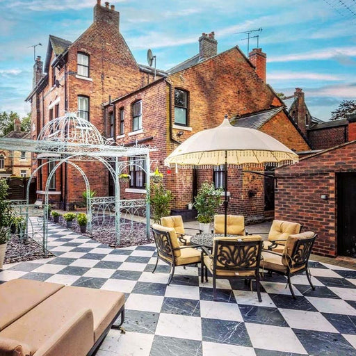 Outdoor courtyard featuring Florence Grand Marquina Black 50x50cm marble-effect porcelain floor tiles, laid in a striking black and white checkerboard pattern and styled with patio seating, parasols and decorative metal structures for a classic yet elegant outdoor entertaining space.