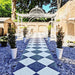 Outdoor garden walkway featuring Florence Grand Calacatta White 50x50cm marble-effect porcelain floor tiles, laid in a striking black and white diamond checkerboard pattern and styled with gravel borders, potted greenery and decorative metal archways for an elegant outdoor statement.