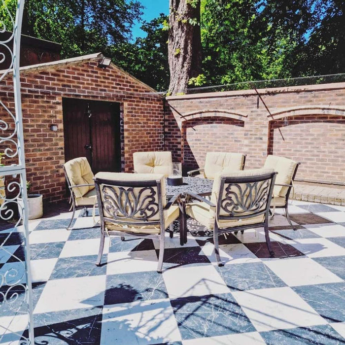Outdoor patio featuring Florence Grand Calacatta White 50x50cm marble-effect porcelain floor tiles, laid in a bold black and white checkerboard pattern and styled with metal garden furniture and exposed brick walls for a timeless, elegant outdoor seating area.