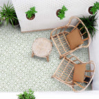 Outdoor patio seating area with rattan chairs, small round table and hanging plants, featuring London Streets Thornton Place Sage Green 20cm x 20cm Victorian Moroccan style patterned floor tiles in a fresh sage and white design.