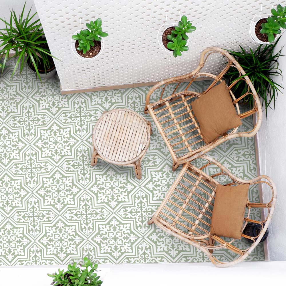 Outdoor patio seating area with rattan chairs, small round table and hanging plants, featuring London Streets Thornton Place Sage Green 20cm x 20cm Victorian Moroccan style patterned floor tiles in a fresh sage and white design.