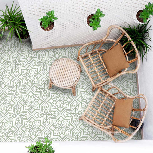 Outdoor patio seating area with rattan chairs, small round table and hanging plants, featuring London Streets Thornton Place Sage Green 20cm x 20cm Victorian Moroccan style patterned floor tiles in a fresh sage and white design.