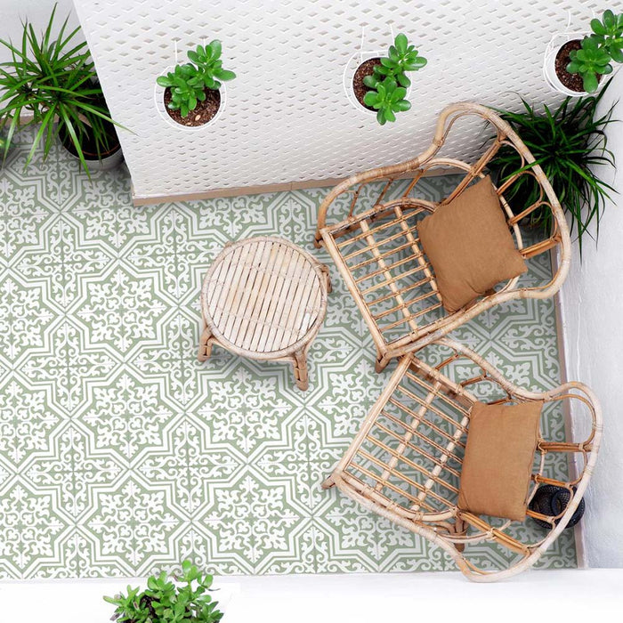 Outdoor patio seating area with rattan chairs, small round table and hanging plants, featuring London Streets Thornton Place Sage Green 20cm x 20cm Victorian Moroccan style patterned floor tiles in a fresh sage and white design.