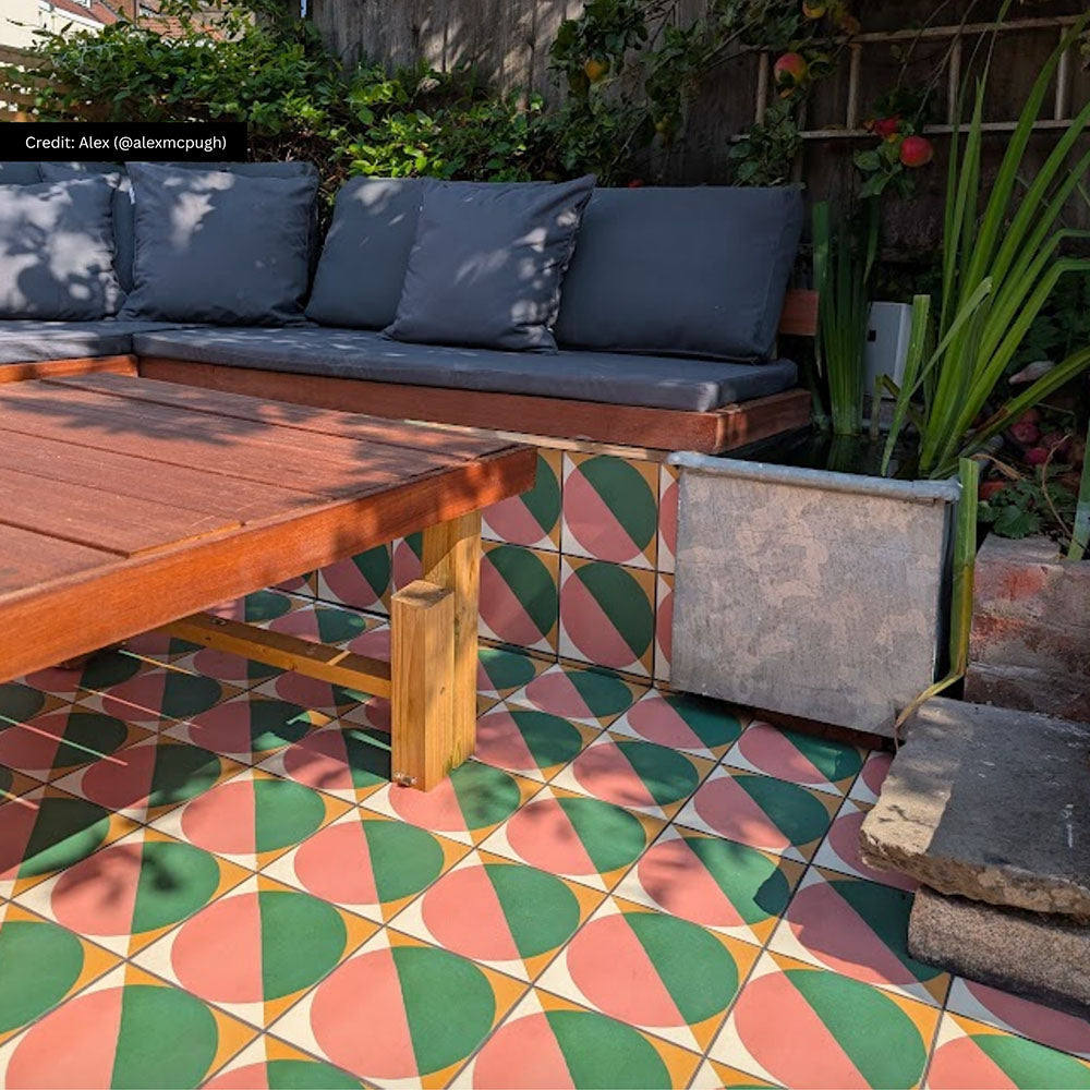Outdoor seating area featuring Abstract Pablo Patterned Tiles in a 20x20cm format, laid as decorative floor tiles beneath a built-in wooden bench. The bold geometric design combines soft pink, deep green and warm ochre tones, creating a playful, modern look that adds colour and character to this garden patio setting.