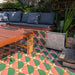 Outdoor seating area featuring Abstract Pablo Patterned Tiles in a 20x20cm format, laid as decorative floor tiles beneath a built-in wooden bench. The bold geometric design combines soft pink, deep green and warm ochre tones, creating a playful, modern look that adds colour and character to this garden patio setting.