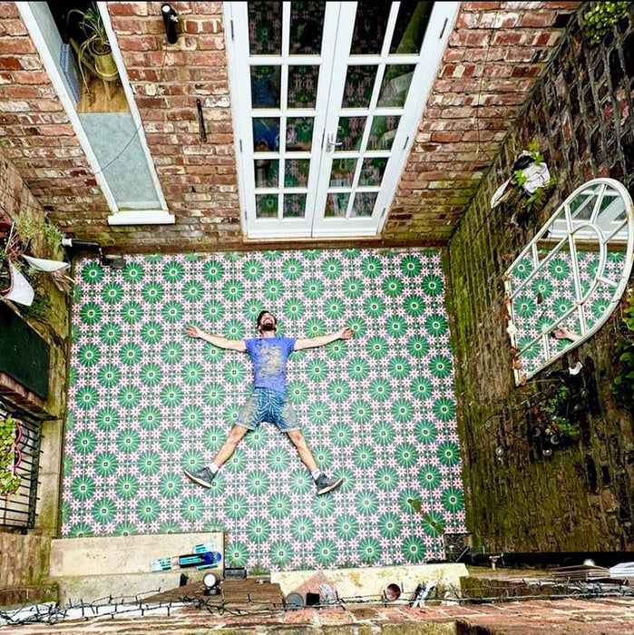 Outdoor courtyard featuring Fez Autumn 20x20cm Moroccan-style porcelain tiles laid across the patio floor, showcasing a bold geometric floral pattern in deep green, blush pink and dark accents, framed by exposed brick walls and French doors for a striking, characterful exterior space.