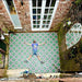 Outdoor courtyard featuring Fez Autumn 20x20cm Moroccan-style porcelain tiles laid across the patio floor, showcasing a bold geometric floral pattern in deep green, blush pink and dark accents, framed by exposed brick walls and French doors for a striking, characterful exterior space.