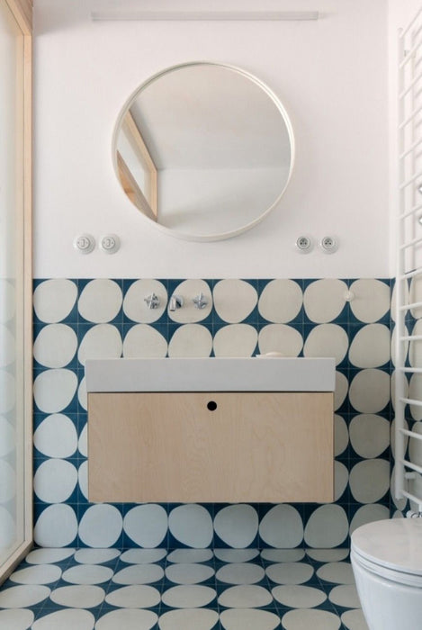 Modern bathroom featuring Pebbles Blue Moroccan style patterned wall and floor tiles in 20cm x 20cm. Bold blue and white geometric circles create a playful statement around a minimalist wood vanity, round mirror and crisp white bathroom fittings.