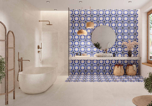 Bathroom featuring Peniscola Blue and Yellow patterned wall and floor tiles, showcasing a bold Mediterranean-inspired floral geometric design in vibrant cobalt blue, warm yellow and crisp white tones, paired with a floating stone vanity, round mirror, woven pendant lights, natural baskets and soft neutral finishes for a bright, characterful interior.