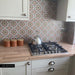 Kitchen featuring Persia Mini Flowers 15x15cm patterned wall tiles used as a splashback, showcasing soft pink, sage green and warm neutral geometric floral motifs, paired with shaker cabinets, oak-effect worktops and a stainless steel gas hob.