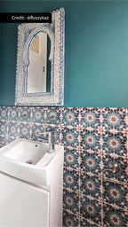 Persia Star Mini 15cm x 15cm Moroccan style tiles, featuring an intricate star pattern in layered blue, teal and warm red tones, used as a statement bathroom wall against rich teal paint and crisp white fixtures.