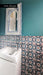 Persia Star Mini 15cm x 15cm Moroccan style tiles, featuring an intricate star pattern in layered blue, teal and warm red tones, used as a statement bathroom wall against rich teal paint and crisp white fixtures.