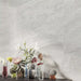 Living room featuring Petra Avorio Ivory stone marble effect porcelain wall tiles in a 60cm x 120cm format, showcasing soft ivory, pearl white and light grey veining inspired by natural stone, paired with colourful glass vases, fresh floral arrangements and contemporary styling to create a bright, elegant interior.
