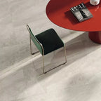 Close-up of Petra Beige stone marble effect porcelain wall and floor tiles in a 30cm x 60cm format, showcasing warm beige, ivory and soft cream veining inspired by natural stone, paired with a contemporary red statement table, green upholstered chair and elegant modern furnishings for a sophisticated interior.
