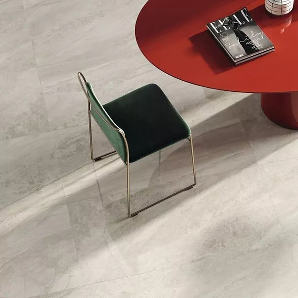 Close-up of Petra Beige stone marble effect porcelain wall and floor tiles in a 30cm x 60cm format, showcasing warm beige, ivory and soft cream veining inspired by natural stone, paired with a contemporary red statement table, green upholstered chair and elegant modern furnishings for a sophisticated interior.