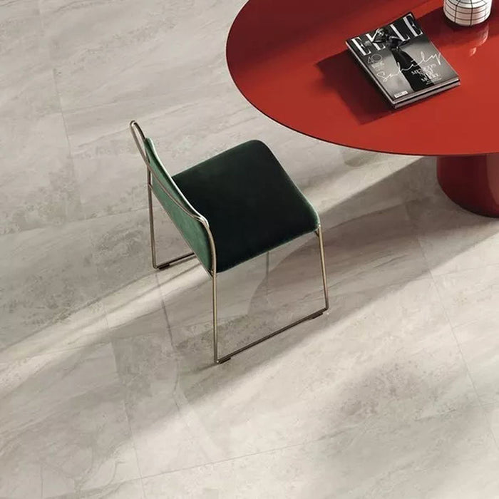 Close-up of Petra Beige stone marble effect porcelain wall and floor tiles in a 30cm x 60cm format, showcasing warm beige, ivory and soft cream veining inspired by natural stone, paired with a contemporary red statement table, green upholstered chair and elegant modern furnishings for a sophisticated interior.