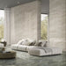 Living room featuring Petra Verde Green stone marble effect porcelain wall tiles in a 30cm x 60cm format, showcasing flowing green, sage and soft grey veining inspired by natural stone, paired with large-format stone effect flooring, floor-to-ceiling windows, soft neutral furnishings and a contemporary open-plan interior.